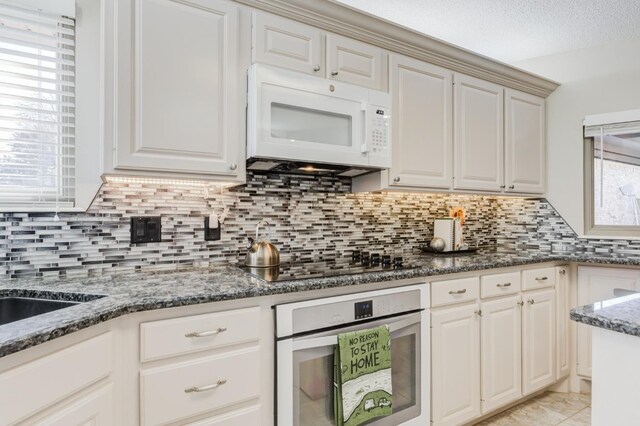 kitchen with light tile patterned floors, decorative backsplash, white appliances, and dark stone counters