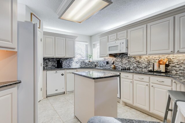 kitchen featuring white appliances, dark stone counters, a kitchen island, and light tile patterned floors