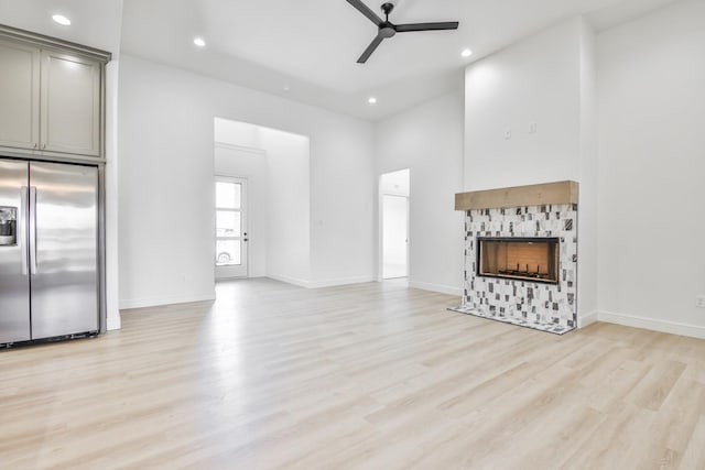 unfurnished living room featuring a towering ceiling, light hardwood / wood-style flooring, a tile fireplace, and ceiling fan