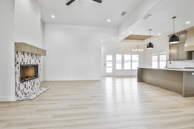 unfurnished living room with ceiling fan, a tray ceiling, a fireplace, and light hardwood / wood-style floors