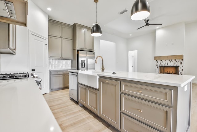 kitchen with sink, stainless steel refrigerator with ice dispenser, decorative backsplash, a center island with sink, and decorative light fixtures