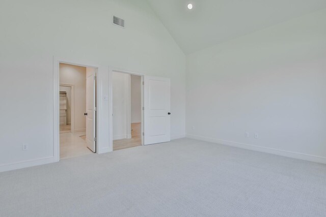 unfurnished bedroom featuring light carpet, high vaulted ceiling, and ensuite bathroom