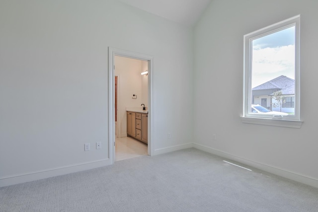 unfurnished bedroom with ensuite bathroom, vaulted ceiling, and light carpet