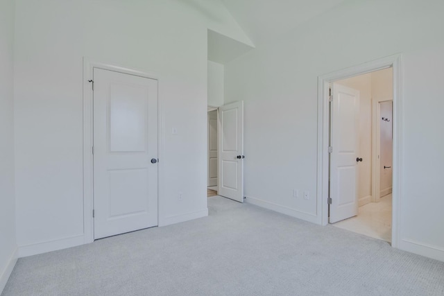 unfurnished bedroom featuring connected bathroom, vaulted ceiling, and light colored carpet