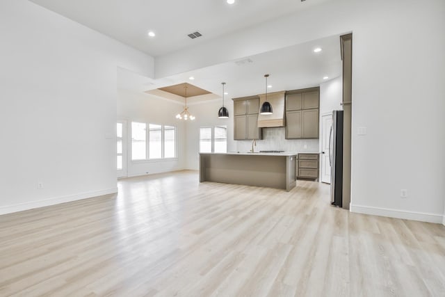 unfurnished living room with sink, a chandelier, light wood-type flooring, and a tray ceiling