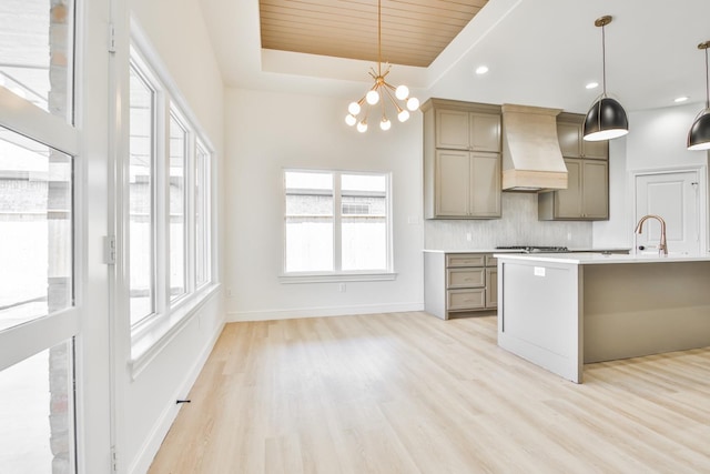 kitchen with light hardwood / wood-style flooring, tasteful backsplash, custom range hood, decorative light fixtures, and a raised ceiling