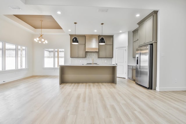 kitchen with wall chimney exhaust hood, a center island with sink, stainless steel fridge, a tray ceiling, and pendant lighting