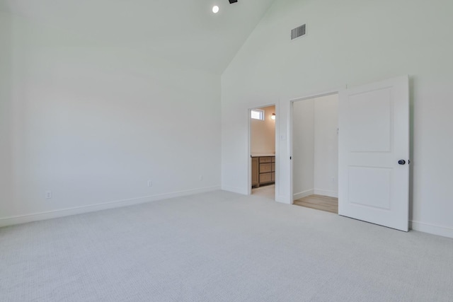 unfurnished bedroom with high vaulted ceiling, light colored carpet, and ensuite bathroom