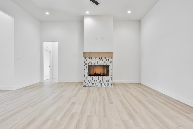 unfurnished living room featuring ceiling fan, a tiled fireplace, and light hardwood / wood-style floors