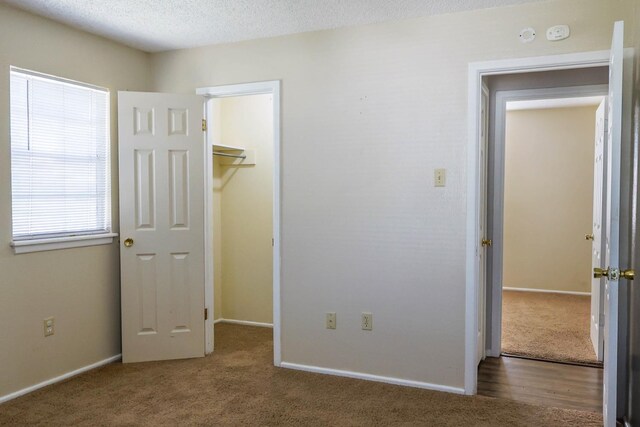 unfurnished bedroom featuring a spacious closet, a textured ceiling, dark carpet, and a closet