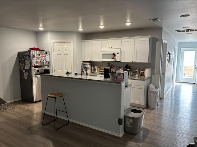 kitchen featuring white cabinetry, stainless steel fridge, a center island with sink, and stone counters