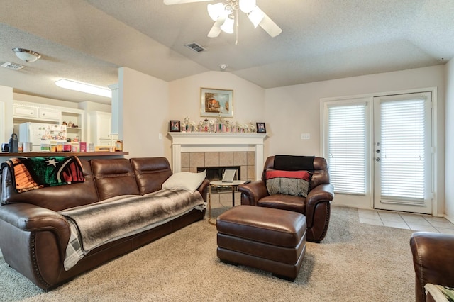 living room with lofted ceiling, ceiling fan, a textured ceiling, a tiled fireplace, and light colored carpet