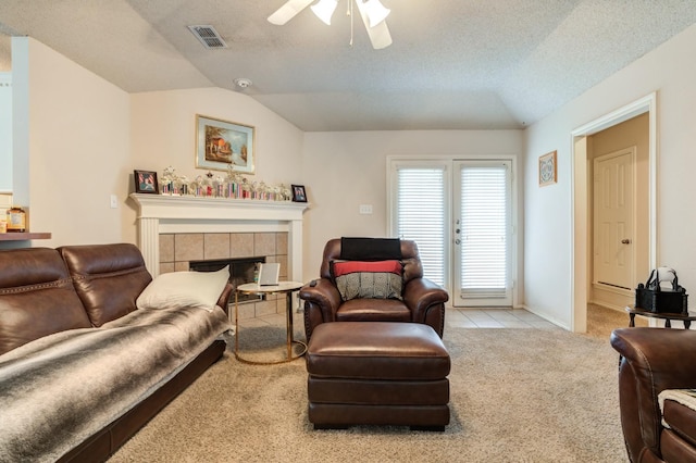 living room featuring lofted ceiling, ceiling fan, a fireplace, a textured ceiling, and light colored carpet