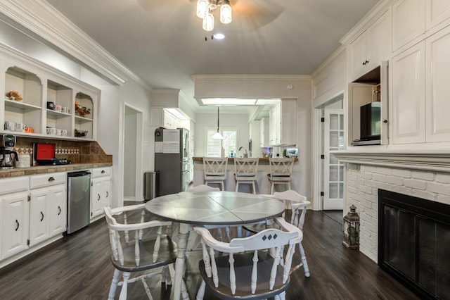 dining area featuring sink, a brick fireplace, crown molding, and dark hardwood / wood-style floors