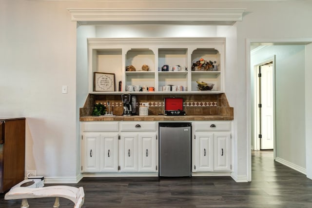 bar featuring dark wood-type flooring, stainless steel refrigerator, and white cabinets