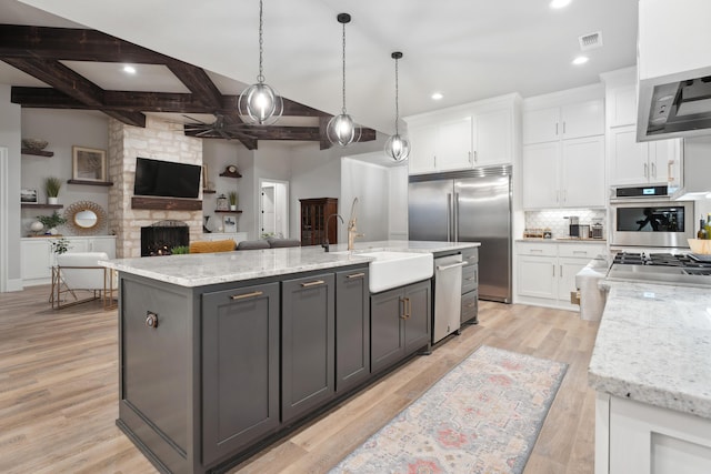 kitchen featuring light stone counters, appliances with stainless steel finishes, pendant lighting, a kitchen island with sink, and white cabinets