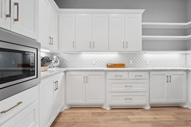 kitchen with light stone counters, stainless steel microwave, light wood-type flooring, and white cabinets