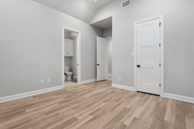 unfurnished bedroom featuring ensuite bath, lofted ceiling, and light wood-type flooring