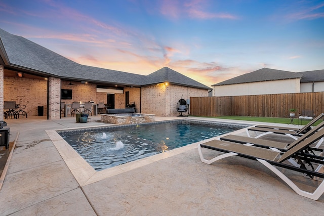 pool at dusk featuring a patio area, an in ground hot tub, pool water feature, and exterior bar