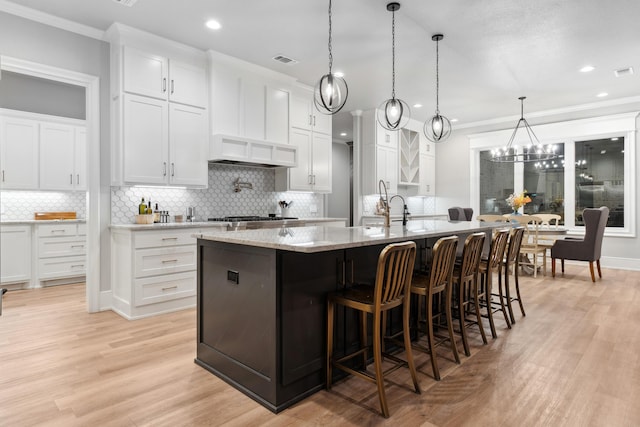 kitchen featuring a large island, hanging light fixtures, light stone counters, white cabinets, and custom exhaust hood