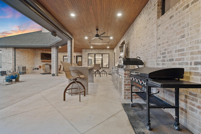 patio terrace at dusk with an outdoor kitchen, central air condition unit, ceiling fan, and a bar