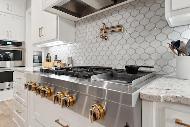 kitchen featuring white cabinetry, stainless steel appliances, light stone counters, tasteful backsplash, and wall chimney exhaust hood