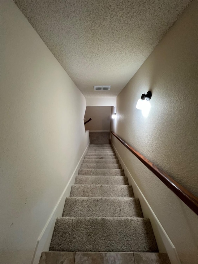 stairway with a textured ceiling and carpet flooring