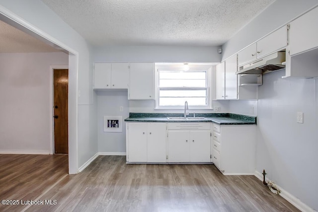 504 53rd St, Lubbock, TX 79404 - kitchen with under cabinet range hood, a textured ceiling, white cabinets, dark countertops, and light wood-style flooring