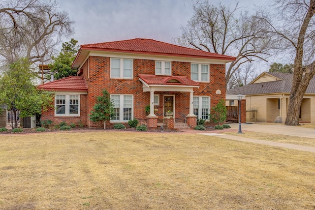 view of front facade with a front yard, a tiled roof, cooling unit, and brick siding