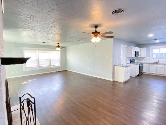 unfurnished living room with sink, a textured ceiling, dark wood-type flooring, and a healthy amount of sunlight