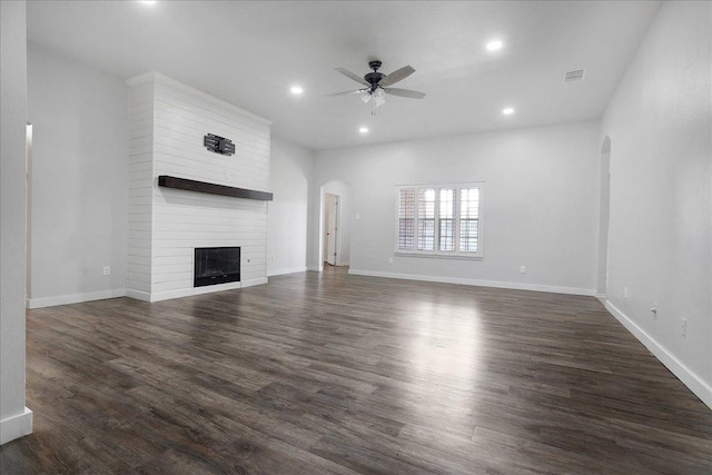 unfurnished living room featuring dark wood-type flooring, a large fireplace, and ceiling fan