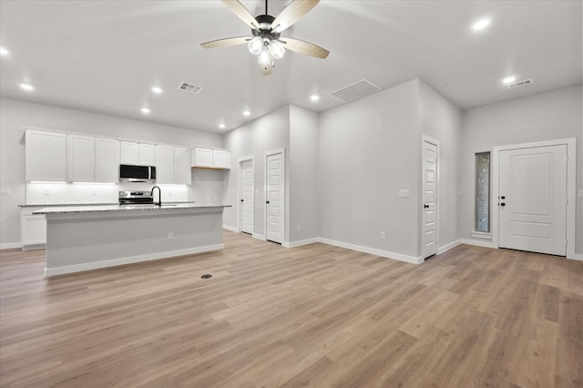 interior space with white cabinetry, ceiling fan, light hardwood / wood-style floors, stainless steel appliances, and a center island with sink