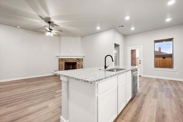 kitchen with white cabinetry, sink, a kitchen island with sink, light stone countertops, and light wood-type flooring