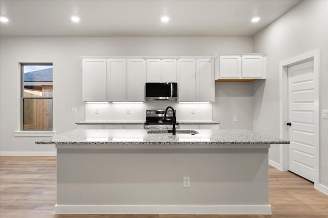 kitchen with sink, white cabinetry, appliances with stainless steel finishes, light stone countertops, and a kitchen island with sink