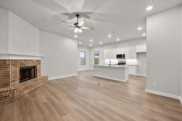 unfurnished living room with ceiling fan, sink, a fireplace, and light hardwood / wood-style floors