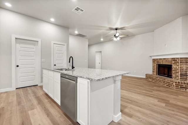 kitchen featuring sink, a brick fireplace, dishwasher, an island with sink, and white cabinets