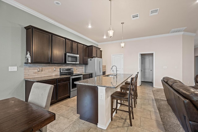 kitchen featuring pendant lighting, sink, stainless steel appliances, light stone countertops, and a center island with sink