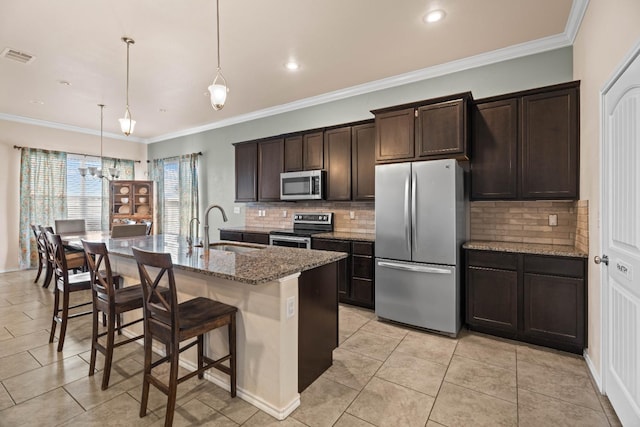 kitchen featuring sink, light stone counters, decorative light fixtures, appliances with stainless steel finishes, and an island with sink