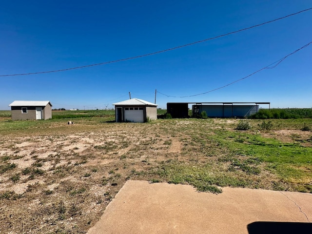 view of yard featuring a rural view, a storage shed, and a garage