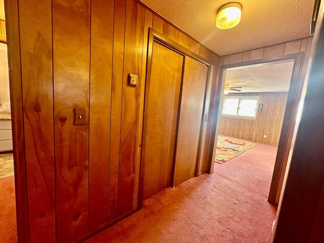 corridor with wooden walls, light carpet, and a textured ceiling