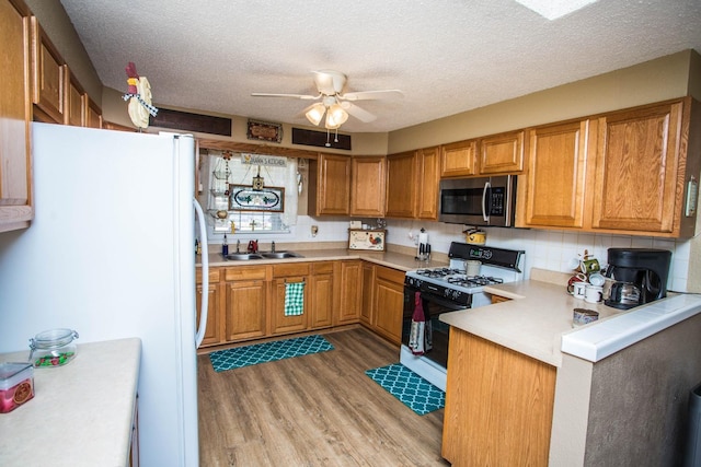 kitchen with sink, light wood-type flooring, white fridge, ceiling fan, and gas range oven