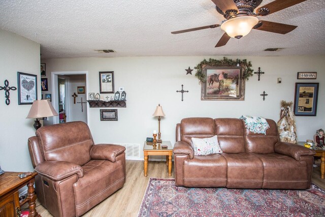 living room with ceiling fan, a textured ceiling, and light hardwood / wood-style floors