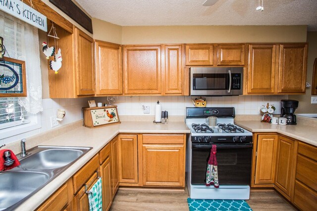 kitchen with sink, backsplash, range with gas cooktop, and light wood-type flooring