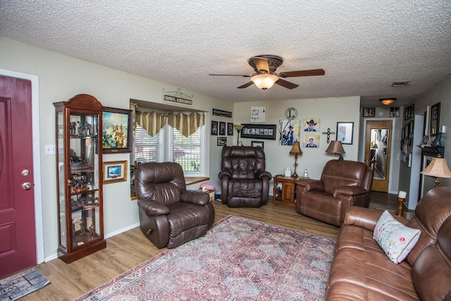 living room with ceiling fan, a textured ceiling, and light wood-type flooring