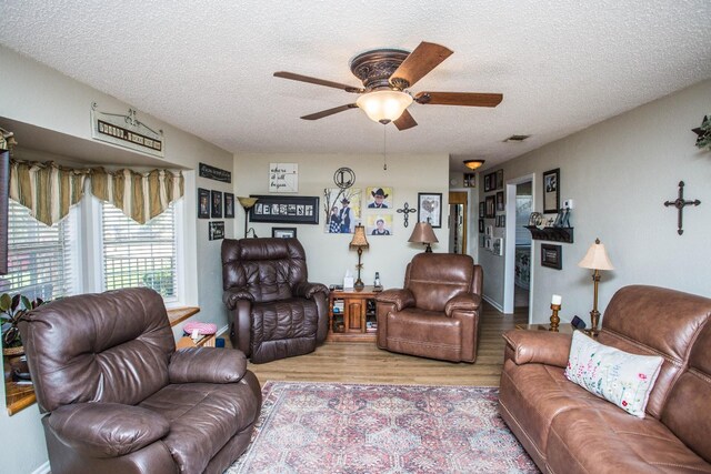 living room featuring ceiling fan, a textured ceiling, and light wood-type flooring