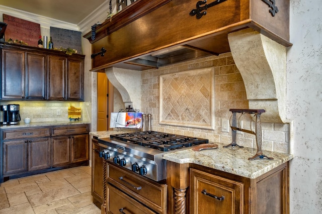 kitchen featuring stainless steel gas stovetop, backsplash, ornamental molding, light stone countertops, and custom range hood