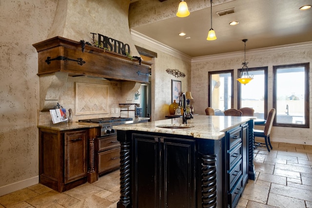 kitchen featuring a kitchen island with sink, sink, pendant lighting, and light stone countertops