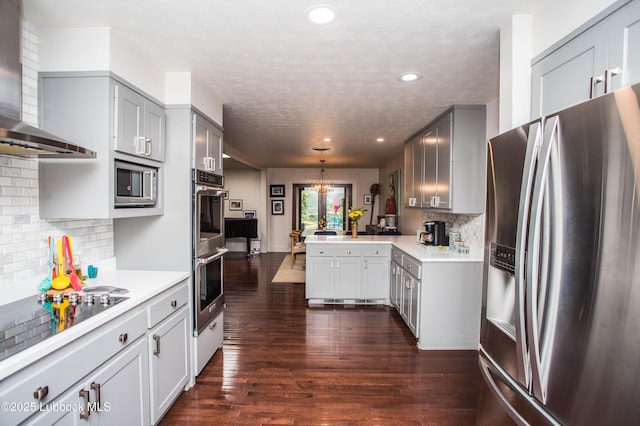 4609 10th St, Lubbock, TX 79416 - kitchen featuring stainless steel appliances, wall chimney exhaust hood, a peninsula, light countertops, and dark wood-style flooring