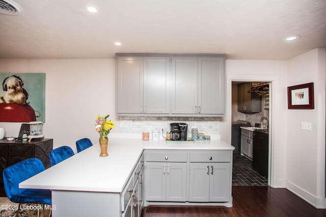 4609 10th St, Lubbock, TX 79416 - kitchen featuring dark wood-style flooring, light countertops, a breakfast bar, backsplash, and a peninsula