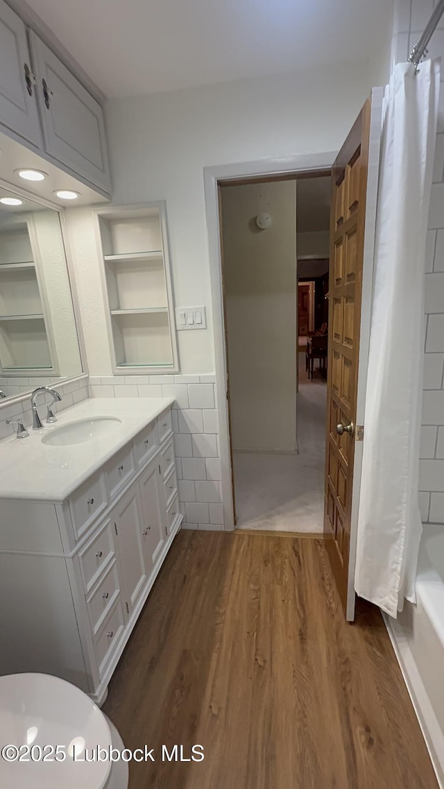 3806 56th St, Lubbock, TX 79413 - bathroom featuring tile walls, vanity, wood finished floors, shower / bath combo with shower curtain, and a wainscoted wall